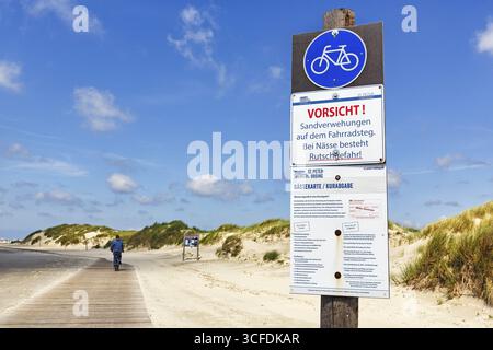 Cycliste sur le chemin en bois à travers les dunes à la mer, signe avertit de l'humidité, danger de glisser et dérives de sable sur la piste cyclable, Cumulus, Sankt Peter-Ord Banque D'Images