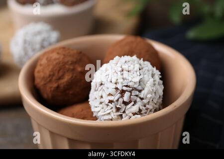 Délicieux bonbons faits maison avec de la poudre de cacao et des flocons de noix de coco dans un bol sur la table, gros plan Banque D'Images