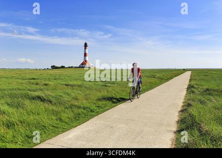 Cycliste, tour à vélo à travers les marais salants, Westerheversand phare à l'horizon, Cirrus, Westerhever, Eiderstedt, Frise du Nord, Schleswig-Holstein Banque D'Images