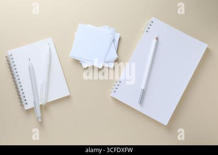Blocs-notes blancs, notes en papier, crayon et stylos sur fond beige, pose à plat Banque D'Images