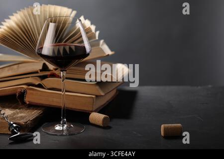 Vin rouge en verre et livres sur table texturée sombre sur fond gris, gros plan. Espace pour le texte Banque D'Images