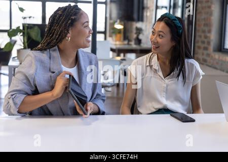 Divers collègues ouvrant l'étui de tablette et discutant à la table blanche dans un bureau moderne avec smartphone Banque D'Images