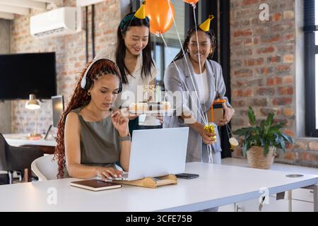 Diverses collègues féminines célébrant l'anniversaire au bureau tenant des cupcakes gâteaux et des cadeaux Banque D'Images