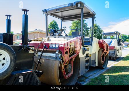 De nombreux engins de construction stationnés en rangée le long d'une rue résidentielle de la ville en été Banque D'Images