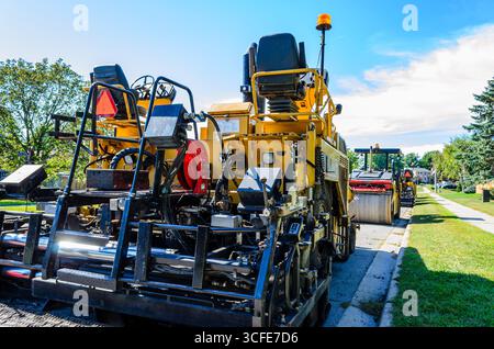 Vue arrière d'un finisseur de route et d'une gamme de matériel de construction sur une rue résidentielle un jour d'été Banque D'Images
