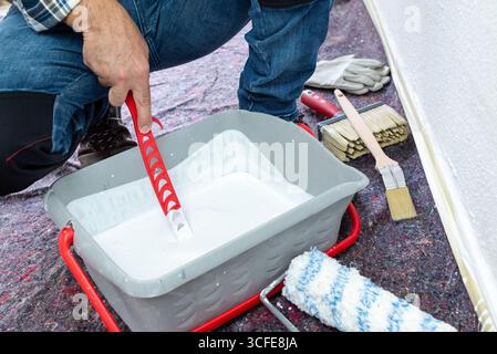 Gros plan d'une main. Un peintre prépare la peinture blanche pour blanchir le mur à la chaux. Industrie de la construction. Banque D'Images