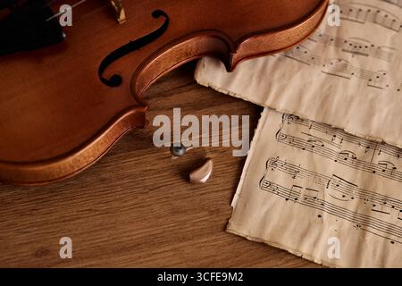 L'aide auditive moderne repose sur une surface en bois avec un violon et une partition, fusionnant musique et santé auditive Banque D'Images