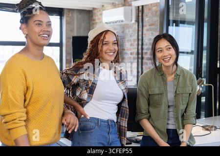 Diverses collègues féminines debout au bureau dans le bureau partageant des mises à jour sur les moniteurs et les smartphones Banque D'Images