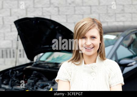 Voiture noire assise avec capot relevé révélant des composants du moteur près d'un mur de briques grises dans le stationnement Banque D'Images