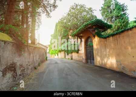 Rue calme étroite à Rome entourée de hauts murs, de verdure et de portes couvertes de lierre Banque D'Images