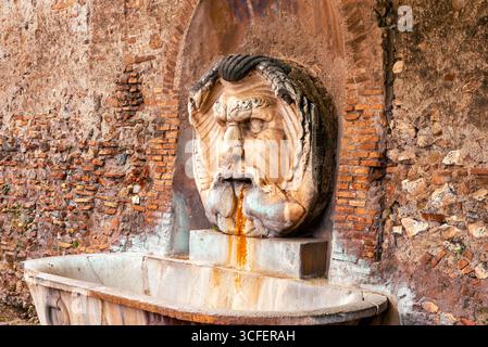 Vieille fontaine en pierre à Rome avec masque sculpté projetant de l'eau contre le mur de briques Banque D'Images