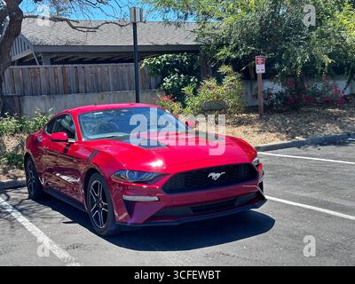 Une voiture de sport Ford Mustang rouge vif garée dans un parking résidentiel par une journée ensoleillée. Le coupé moderne présente un design élégant, des jantes en alliage noir, un Banque D'Images