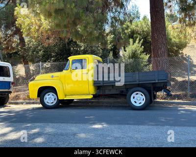 Camion à plateau jaune vintage garé sous les pins sur une rue ensoleillée en Californie Banque D'Images