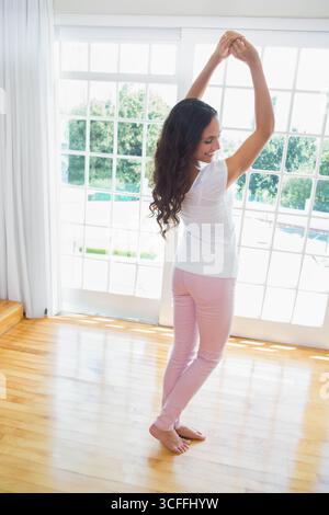 Femme étirant les bras au-dessus de la tête dans le salon avec des portes françaises lambrissées de verre et plancher de bois Banque D'Images