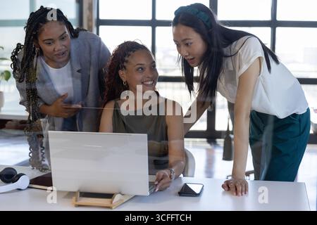 Diverses collègues féminines collaborant autour d'un ordinateur portable et d'un smartphone au bureau avec casque VR Banque D'Images