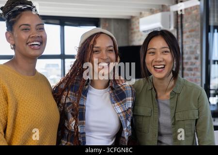 Diverses collègues féminines debout dans le salon de bureau riant et parlant devant le moniteur et les fenêtres Banque D'Images