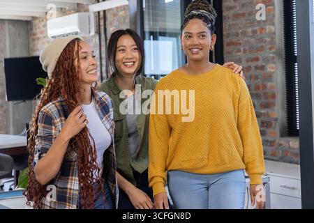 Diverses collègues féminines debout et souriantes au bureau avec des écrans d'ordinateur et des chaises de bureau Banque D'Images