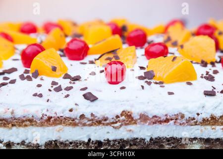 Gâteau crémeux en couches avec des morceaux de chocolat, de cerise et de pêche sur le dessus. Banque D'Images