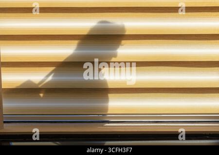 Silhouette d'une personne portant un sac, coulée sur un volet rayé horizontalement pendant l'heure dorée. Banque D'Images