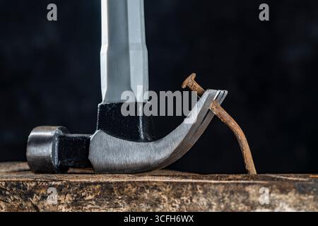 À l'aide d'un marteau pour extraire un vieux clou rouillé d'une planche de bois sur un fond sombre dans l'atelier, gros plan. Outil à main pour travailler Banque D'Images
