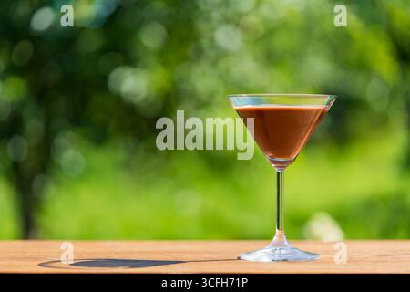 Délicieux cocktail de martini au chocolat servi dans un élégant verre avec un fond de jardin d'été vert, gros plan, espace copie. Parfait pour les fêtes en plein air Banque D'Images