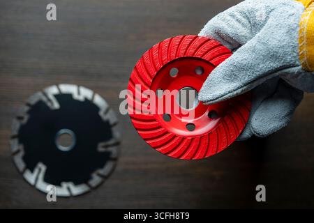 Main d'ouvrier dans des gants de construction tenant le nouveau disque diamant rouge pour meuler le béton, gros plan Banque D'Images