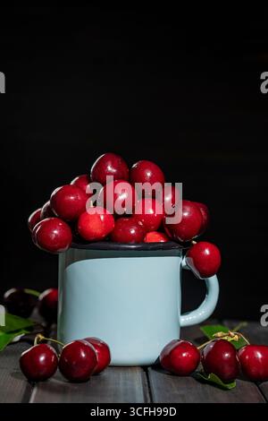 Savoureuses cerises rouges mûres dans un mug bleu métal sur une table en bois. Cerise douce fraîche, gros plan Banque D'Images