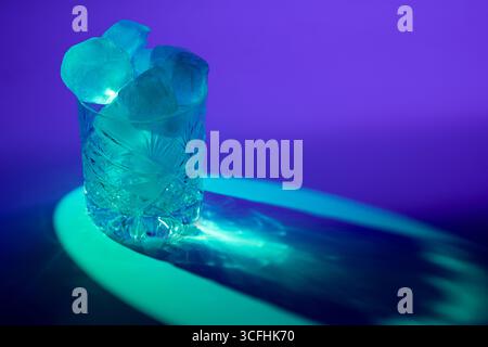 Une photo frappante d'un verre de whisky coupé rempli de glace, illuminé par un rétroéclairage bleu, mettant en valeur la texture glacée et le design élégant du verre Banque D'Images