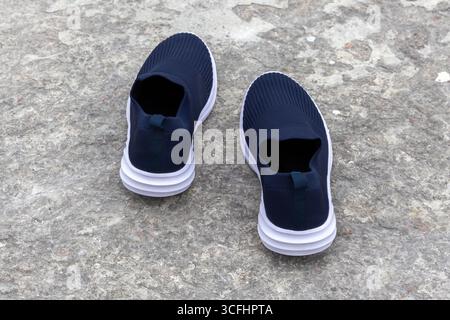 Une paire de baskets à enfiler pour femme. Chaussures confortables et à la mode pour dames, placées sur un sol en béton, vue arrière. Banque D'Images