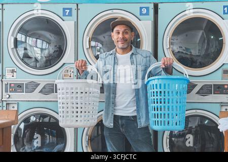 Client tenant deux paniers à linge tout en utilisant des lave-linge en libre-service dans une laverie automatique Banque D'Images