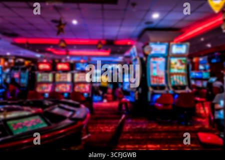 Vue floue de l'intérieur d'un casino avec des machines à sous, des néons et des tables de roulette, créant un fond de vie nocturne atmosphérique. Banque D'Images