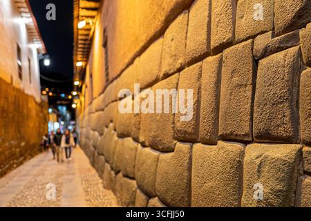 Vue nocturne de la rue Hatun Rumiyoc à Cusco, Pérou, avec les célèbres murs de pierre Inca et les touristes marchant le long de l'allée pavée historique. Banque D'Images