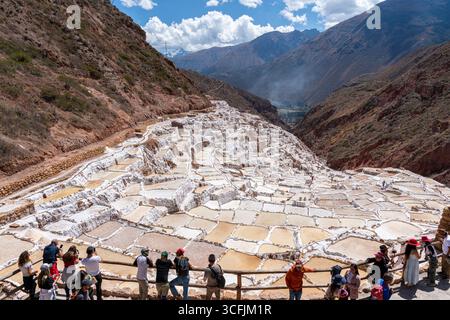 Touristes visitant les étangs salants de Maras à Cusco, Pérou. Attraction de la vallée sacrée avec piscines d'évaporation en terrasse, patrimoine culturel et vues panoramiques. Banque D'Images