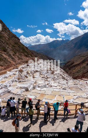 Touristes admirant les mines de sel de Maras à Cusco, Pérou. Vue panoramique sur les étangs d'évaporation en terrasses dans la Vallée sacrée, patrimoine emblématique et landmar inca Banque D'Images