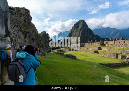 Les touristes se promènent à travers les ruines du Machu Picchu avec les terrasses inca et la montagne Huayna Picchu, le paysage des Andes et le site du patrimoine du Pérou Banque D'Images
