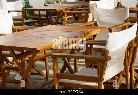 Une disposition de sièges extérieurs confortable avec des tables en bois et des chaises en tissu blanc, mis en place dans un jardin paisible, éclairé par la douceur du milieu de la matinée Banque D'Images