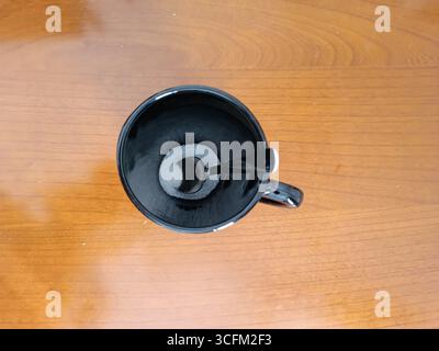 Une tasse à café noire avec une cuillère repose sur une table en bois texturé vide de sucre Banque D'Images