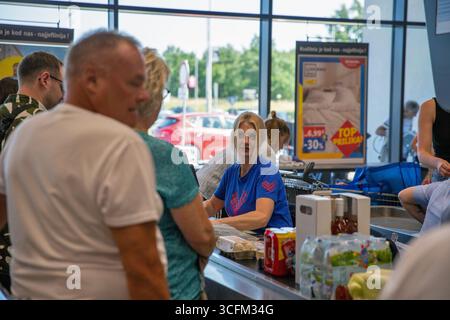 Porec, Croatie - 31 mai 2025 : caissière en uniforme bleu aidant les clients à la caisse dans l'épicerie moderne Lidl. Scène de supermarché occupé avec Banque D'Images