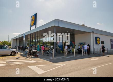 Porec, Croatie - 31 mai 2025 : façade moderne de l'épicerie Lidl avec logo bleu et jaune distinctif. Acheteurs entrant dans le magasin avec des voitures garées, bicyc Banque D'Images