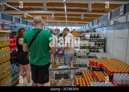 Porec, Croatie - 31 mai 2025 : les acheteurs parcourent la section des boissons dans le supermarché moderne Lidl avec des canettes de bière empilées et des bouteilles. Épicerie très fréquentée Banque D'Images