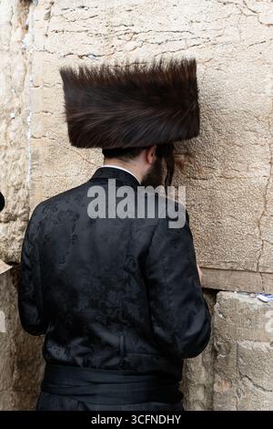 Un juif orthodoxe portant un grand streimel de fourrure prie à côté des pierres anciennes du mur occidental ou Kotel à Jérusalem, Israël. Banque D'Images
