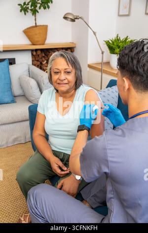 Femme hispanique senior recevant une injection vaccinale, infirmier pratiquant une injection à domicile Banque D'Images
