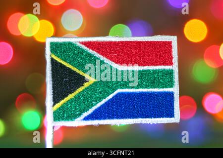 Broderie de drapeau d'Afrique du Sud sur un fond festif, arc-en-ciel bokeh, idéal pour les vacances, le nouvel an ou les fêtes de Noël. Banque D'Images