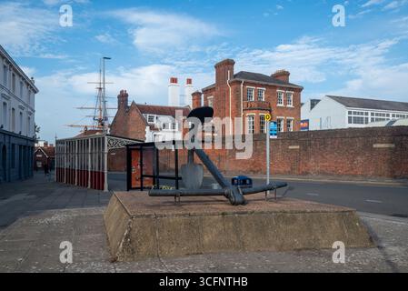 Ancre historique et abri de bus devant l'entrée du chantier naval historique de Portsmouth, avec les mâts du HMS Warrior en arrière-plan. Banque D'Images