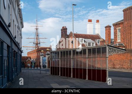Ancien et historique abri de bus en face de l'entrée du chantier naval historique de Portsmouth, avec les mâts du HMS Warrior en arrière-plan. Banque D'Images