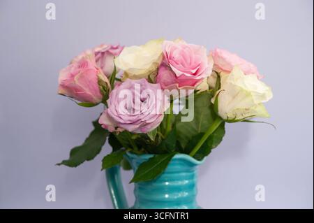 Bouquet de roses colorées dans un vase en céramique turquoise sur fond violet clair Banque D'Images