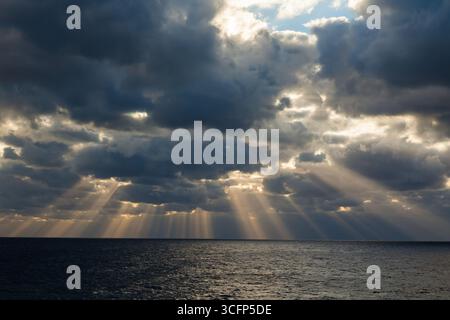 Les rayons du soleil font leur chemin à travers le ciel nuageux couvert en pleine mer. Banque D'Images