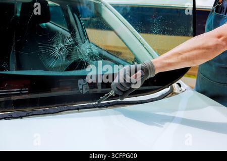 Le technicien utilise des outils pour réparer le pare-brise fissuré d'un véhicule dans un atelier automobile lors du remplacement du pare-brise endommagé Banque D'Images