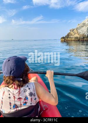 Photo inclinée verticale, femme pagayant un kayak dans le coin inférieur gauche, falaises au-dessus sur la droite, et grand espace ouvert de mer et ciel. Banque D'Images