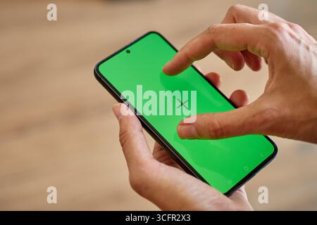 Mains tenant le smartphone et l'écran tactile avec écran vert et marqueurs de suivi. Personne utilisant un téléphone portable, gros plan Banque D'Images